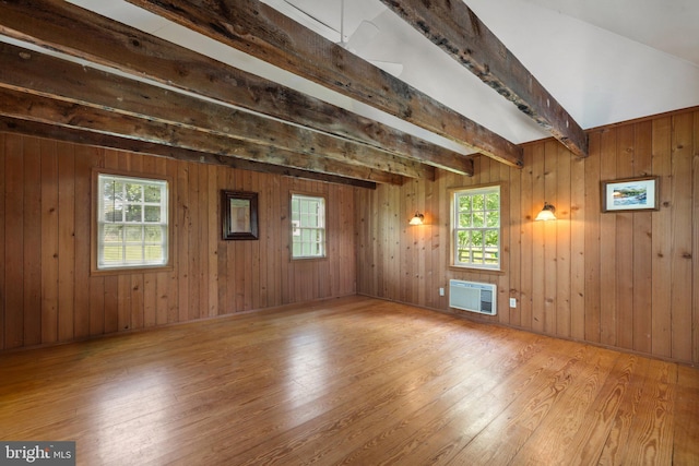 unfurnished room with wood-type flooring, plenty of natural light, beam ceiling, and wooden walls