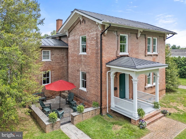 rear view of property featuring a standing seam roof, metal roof, a chimney, a porch, and brick siding