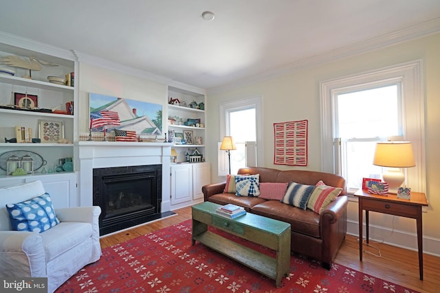 living area with built in shelves, ornamental molding, wood finished floors, and a fireplace