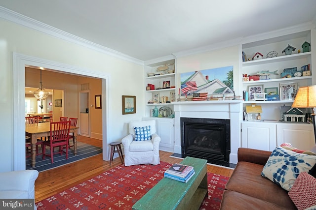 living room featuring crown molding, a fireplace with flush hearth, built in features, and wood finished floors