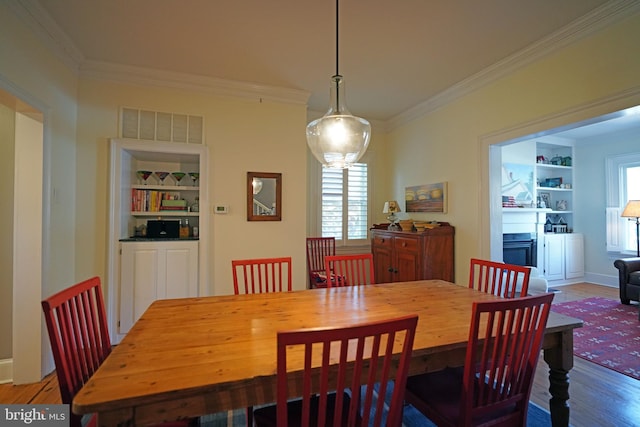 dining space with ornamental molding, a fireplace, light wood-style flooring, and visible vents