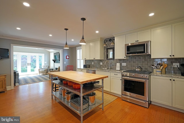 kitchen with appliances with stainless steel finishes, a healthy amount of sunlight, light wood-style flooring, and tasteful backsplash