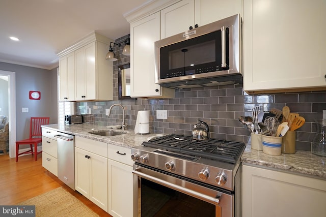 kitchen featuring decorative backsplash, ornamental molding, light wood-style floors, a sink, and stainless steel appliances