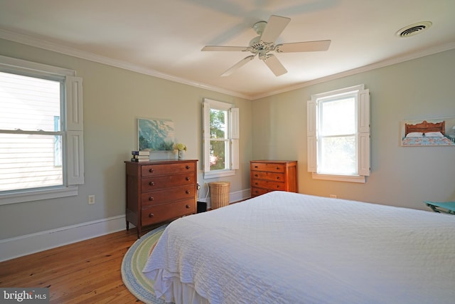 bedroom with light wood-style floors, crown molding, multiple windows, and visible vents