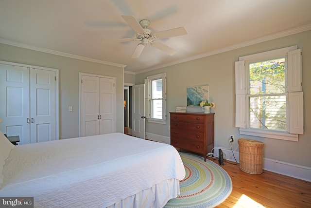 bedroom with two closets, crown molding, baseboards, and light wood-style floors