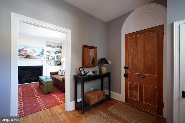 entryway featuring baseboards, a glass covered fireplace, and wood finished floors