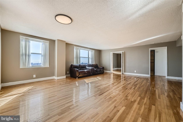 unfurnished living room featuring a wealth of natural light, light wood-style flooring, and baseboards