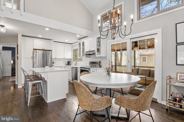 dining room with a notable chandelier, high vaulted ceiling, dark wood-type flooring, baseboards, and recessed lighting