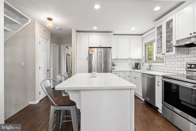 kitchen featuring under cabinet range hood, a breakfast bar area, stainless steel appliances, and dark wood-style flooring