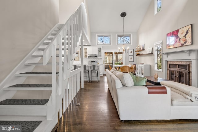 living area featuring stairs, high vaulted ceiling, dark wood-type flooring, a chandelier, and a glass covered fireplace