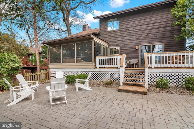 back of house with a deck, a sunroom, a patio area, and a chimney