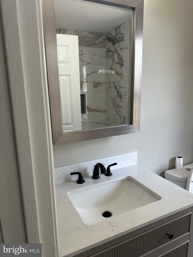 full bathroom with a marble finish shower, toilet, and vanity