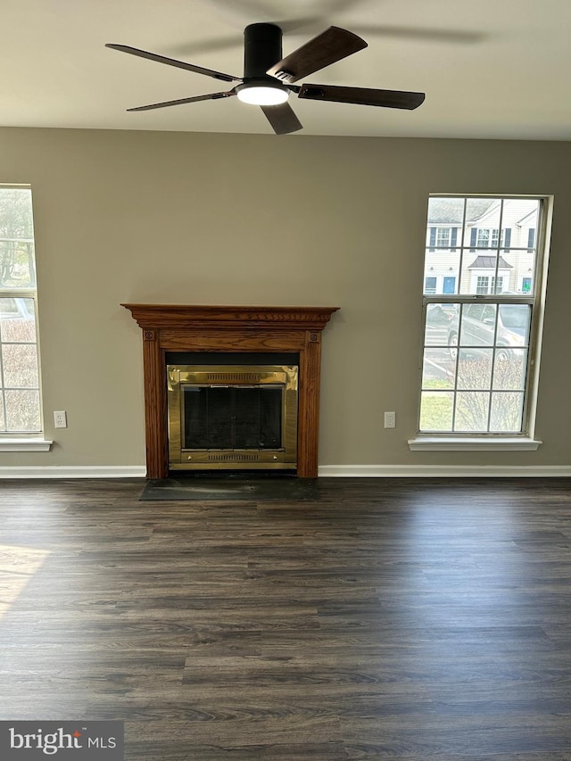 unfurnished living room featuring baseboards, dark wood-type flooring, a healthy amount of sunlight, and ceiling fan