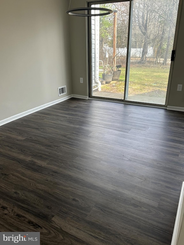 spare room featuring visible vents, baseboards, and dark wood finished floors