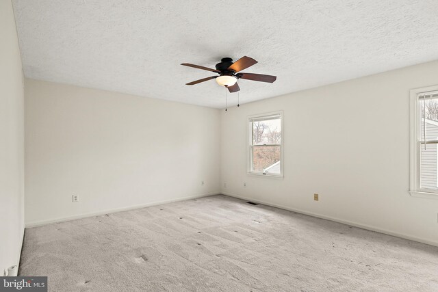 empty room with carpet floors, a textured ceiling, baseboards, visible vents, and ceiling fan