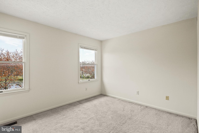 carpeted spare room featuring baseboards, visible vents, and a textured ceiling