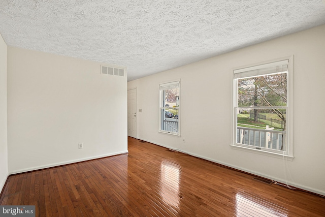 spare room with hardwood / wood-style floors, a textured ceiling, baseboards, and visible vents
