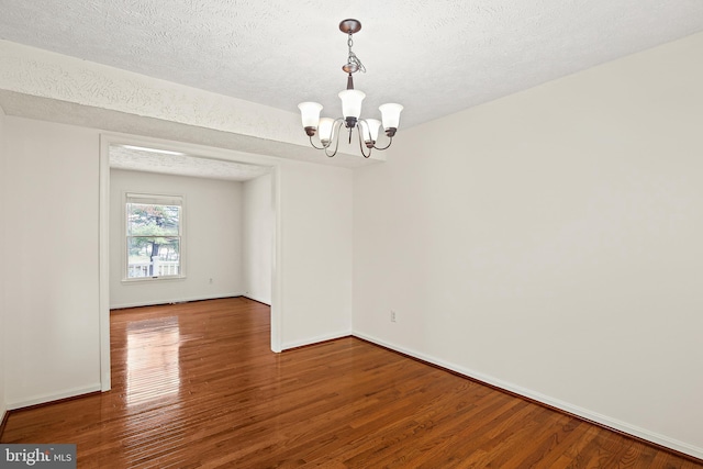 empty room with an inviting chandelier, a textured ceiling, baseboards, and wood finished floors