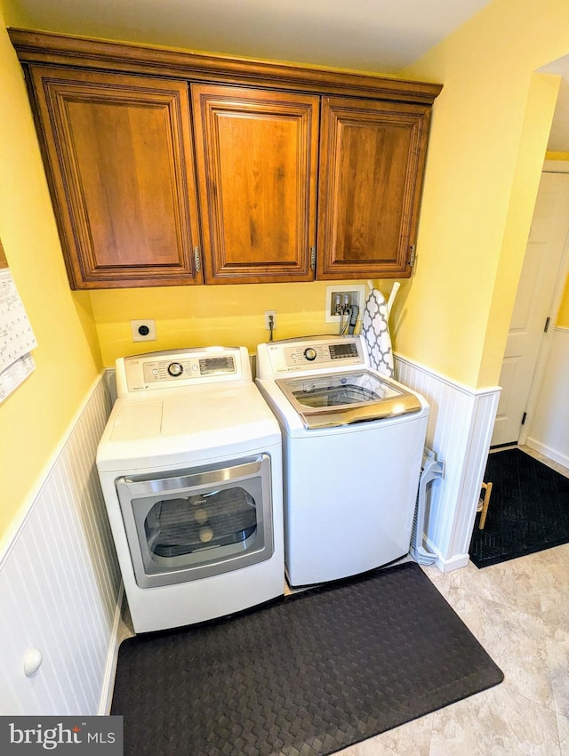 clothes washing area featuring washing machine and clothes dryer, a wainscoted wall, and cabinet space