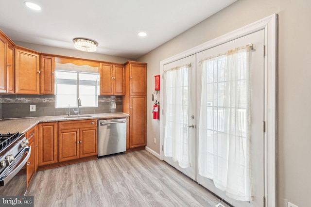 kitchen featuring tasteful backsplash, light wood-type flooring, appliances with stainless steel finishes, brown cabinetry, and a sink