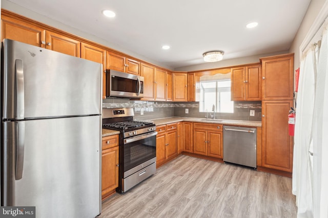 kitchen featuring light wood finished floors, a sink, decorative backsplash, stainless steel appliances, and brown cabinets