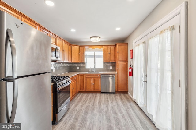 kitchen featuring a sink, light countertops, light wood-style floors, appliances with stainless steel finishes, and backsplash