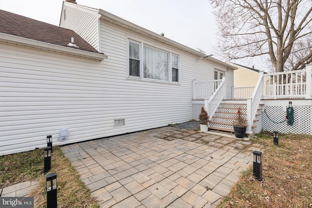 rear view of house featuring a wooden deck, roof with shingles, and a patio area