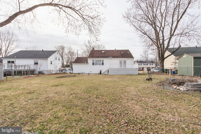 back of property with an outbuilding, a lawn, a chimney, and fence