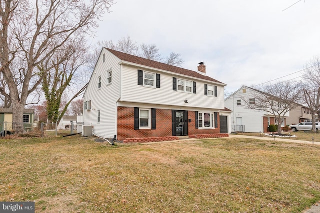 colonial-style house with fence, cooling unit, a front yard, brick siding, and a chimney