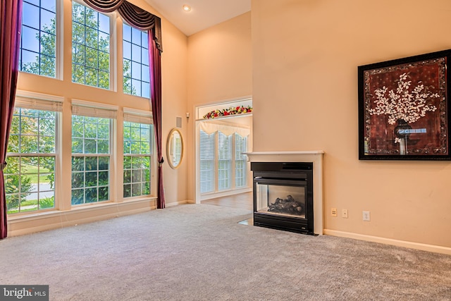 unfurnished living room featuring a high ceiling, carpet floors, a multi sided fireplace, and baseboards