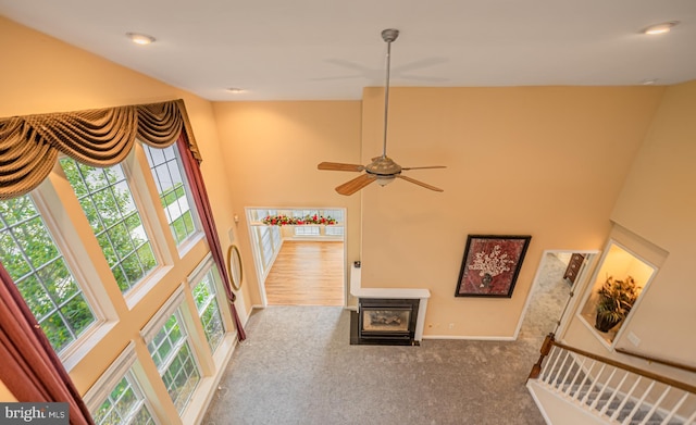 living area with plenty of natural light, ceiling fan, a towering ceiling, carpet flooring, and baseboards