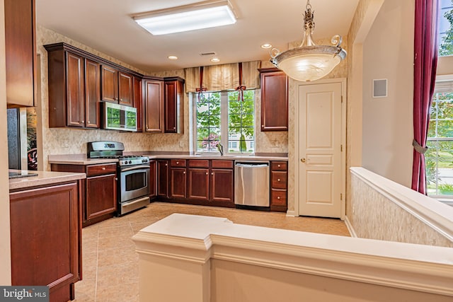 kitchen with appliances with stainless steel finishes, tasteful backsplash, light countertops, a sink, and pendant lighting
