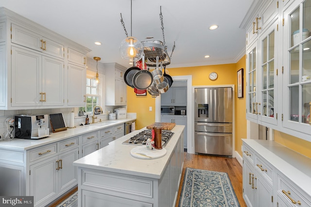 kitchen featuring glass insert cabinets, a kitchen island, a sink, stainless steel appliances, and light wood finished floors