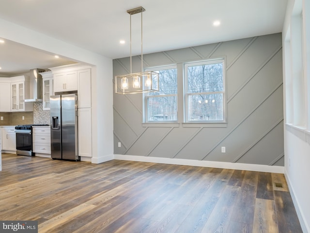 interior space featuring wood finished floors, stainless steel appliances, white cabinets, wall chimney range hood, and backsplash