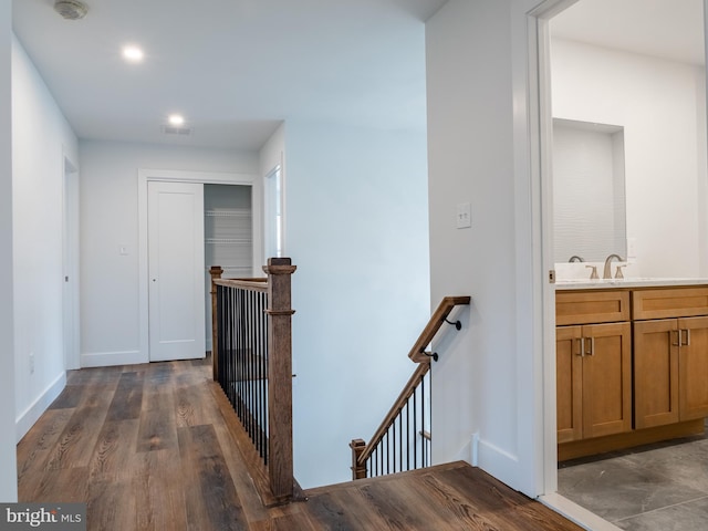 hallway featuring visible vents, baseboards, an upstairs landing, dark wood-style floors, and a sink