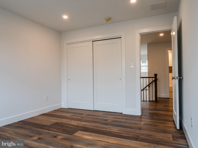 unfurnished bedroom featuring a closet, visible vents, baseboards, and dark wood-style flooring