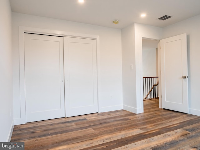 unfurnished bedroom with a closet, visible vents, baseboards, and wood finished floors