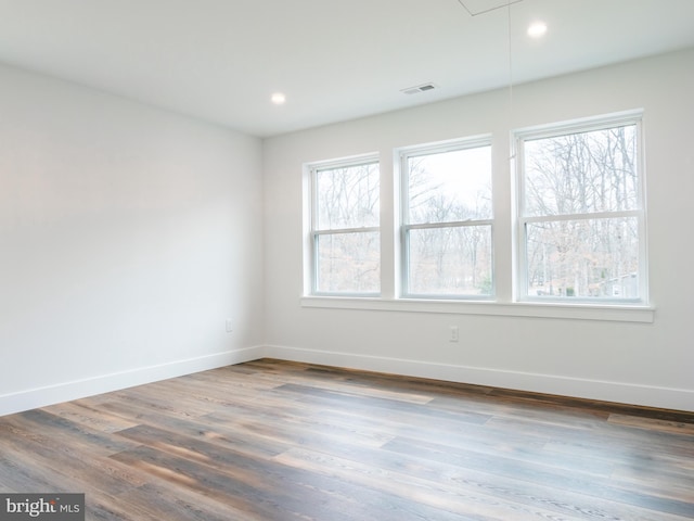 spare room featuring attic access, wood finished floors, baseboards, and a healthy amount of sunlight