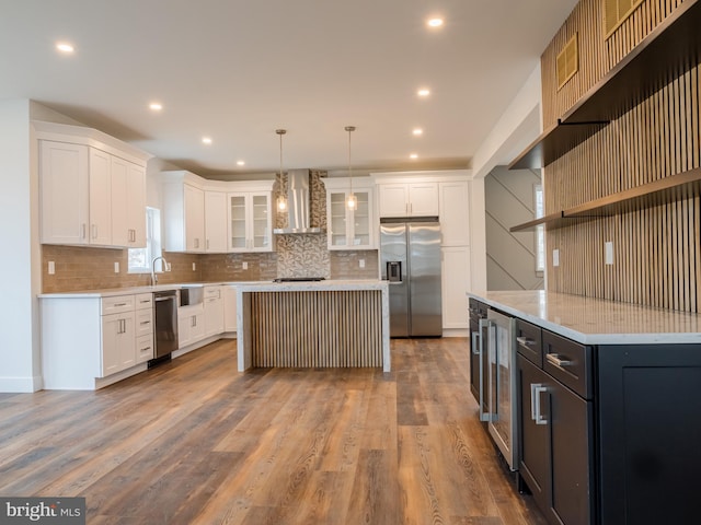 kitchen featuring wall chimney range hood, wood finished floors, stainless steel fridge, and white cabinets