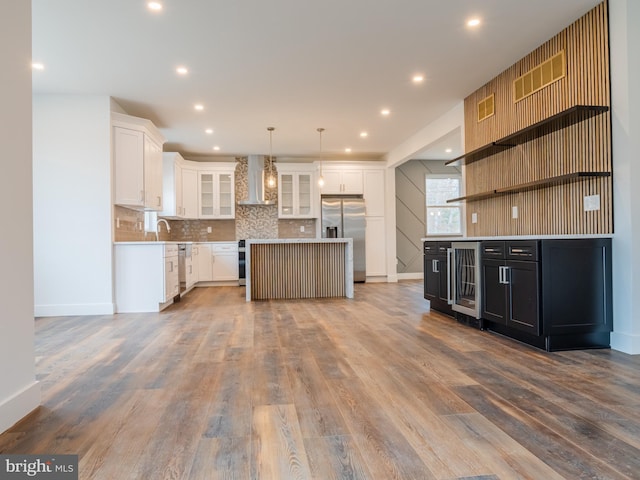 kitchen featuring wood finished floors, beverage cooler, open shelves, appliances with stainless steel finishes, and wall chimney range hood