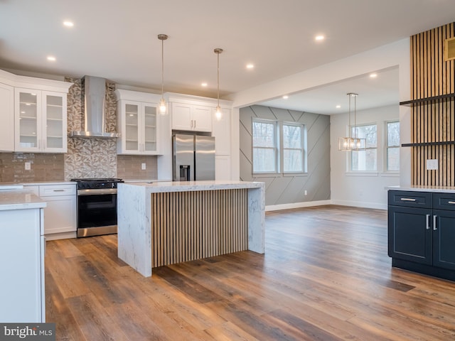 kitchen with stainless steel fridge, gas stove, white cabinets, and wall chimney range hood