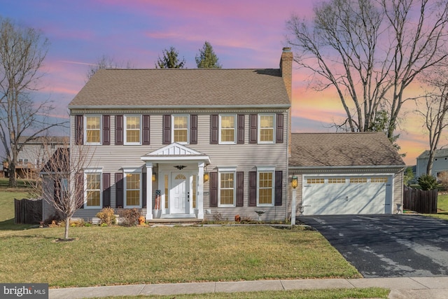 view of front of house featuring a front lawn, driveway, an attached garage, a shingled roof, and a chimney