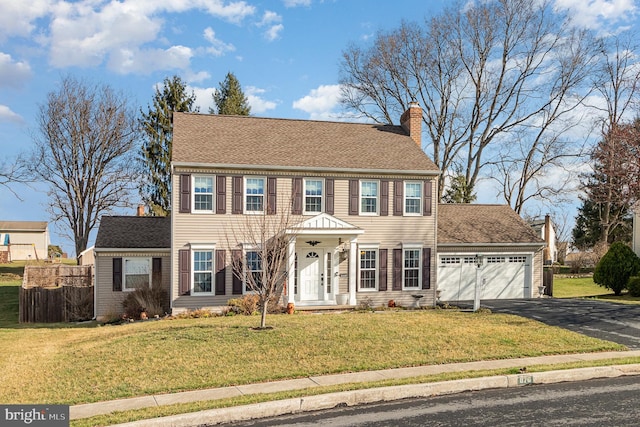 colonial-style house with aphalt driveway, a front yard, a garage, and a chimney