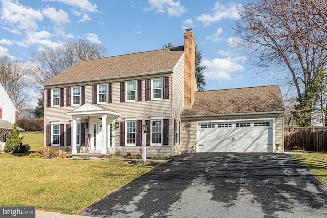 colonial home featuring fence, aphalt driveway, a front yard, a chimney, and a garage