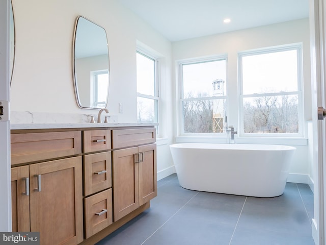 full bath featuring tile patterned flooring, baseboards, recessed lighting, a freestanding tub, and vanity