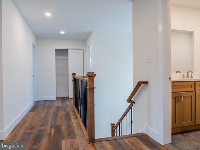 hall with an upstairs landing, baseboards, dark wood-style flooring, and a sink