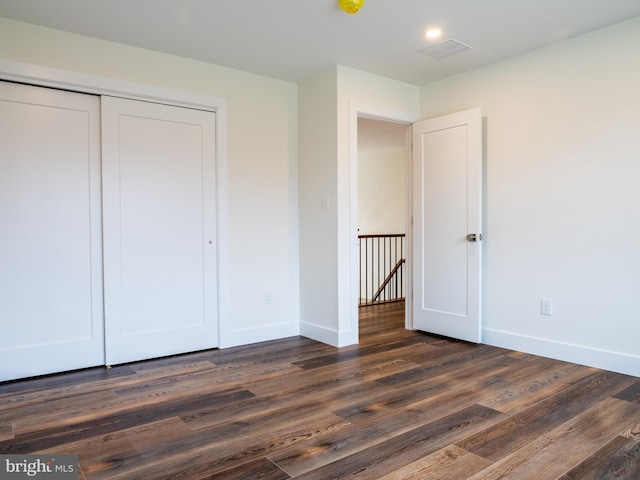 unfurnished bedroom with a closet, baseboards, visible vents, and dark wood-style flooring