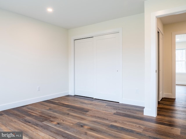 unfurnished bedroom featuring a closet, baseboards, and dark wood-type flooring