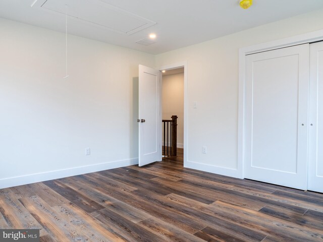 unfurnished bedroom featuring a closet, baseboards, attic access, and dark wood-style flooring