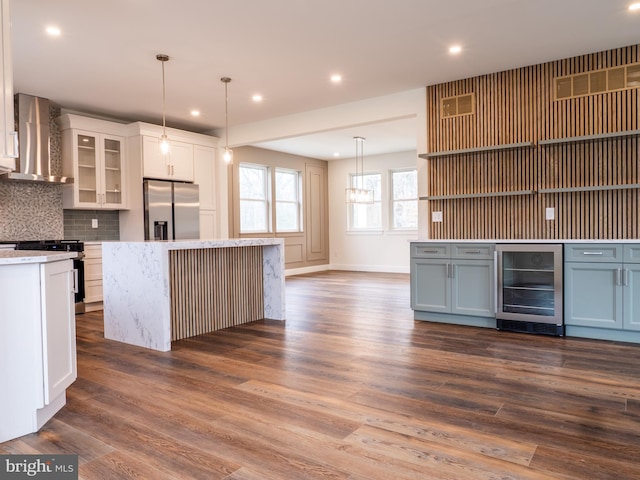 kitchen with backsplash, dark wood-type flooring, wall chimney range hood, wine cooler, and appliances with stainless steel finishes